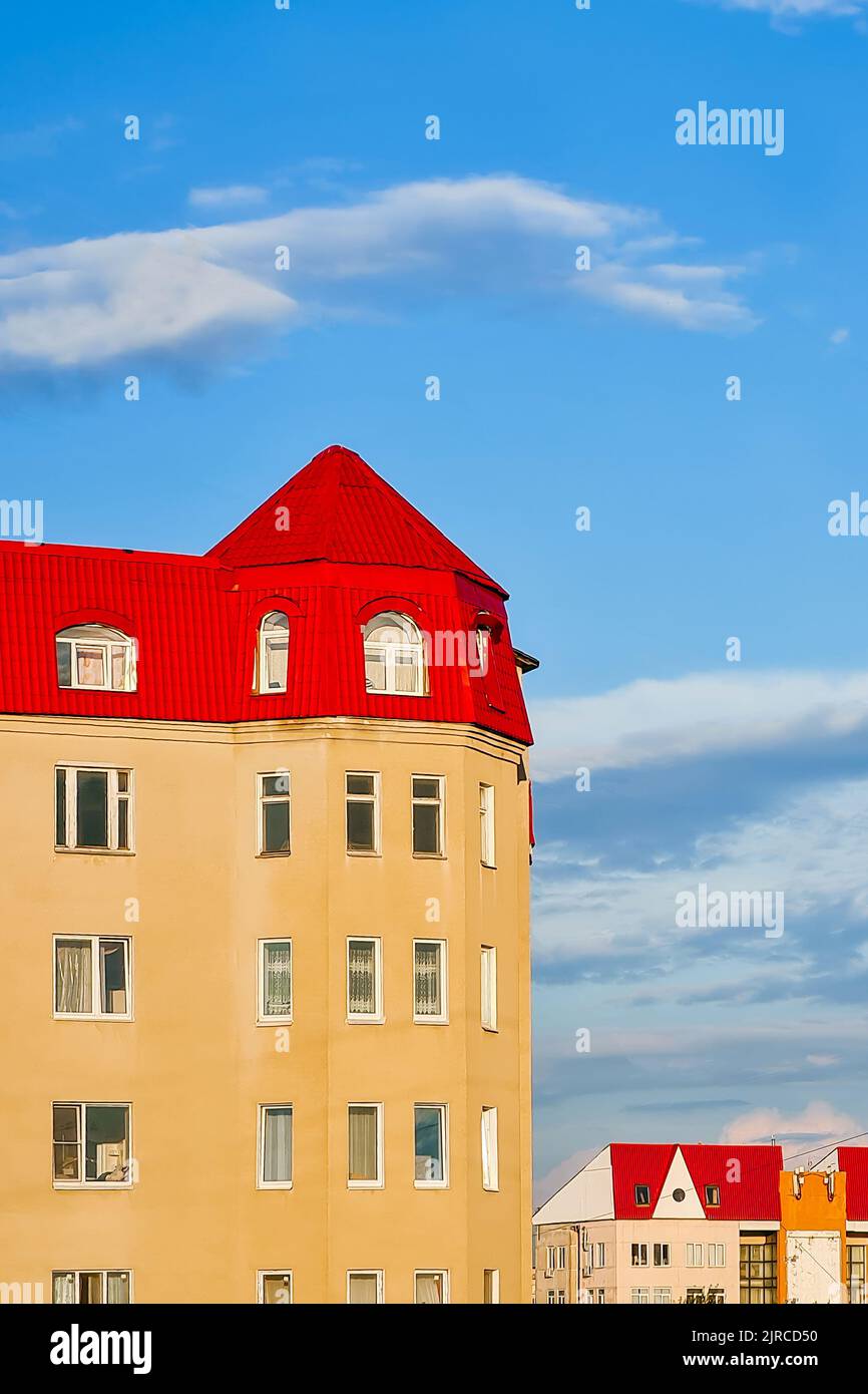 Hohes Wohngebäude mit rotem Ziegeldach vor blauem Himmel. Luftaufnahme, vertikales Foto. Stockfoto