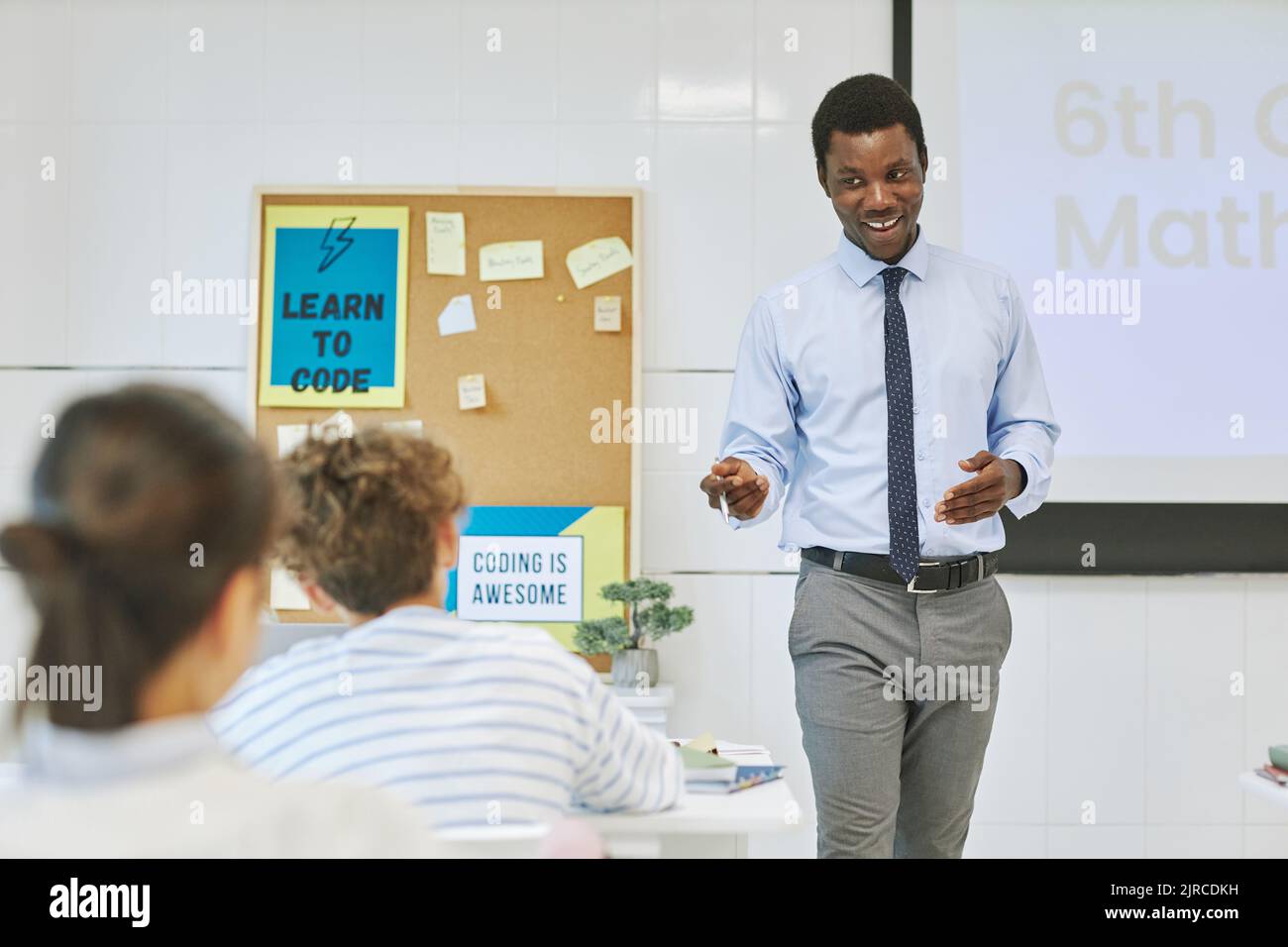 Porträt eines jungen schwarzen Lehrers, der fröhlich im Unterricht lächelt, während er den Kindern das Thema vorstellt Stockfoto