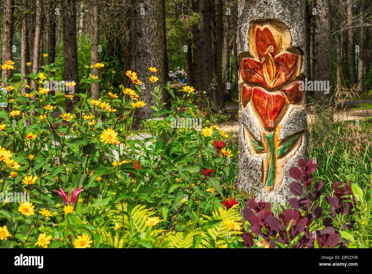 Eine Blumenholzschnitzerei auf einem Totempfahl in einem Blumengarten im Riding Mountain National Park, Manitoba, Kanada. Stockfoto