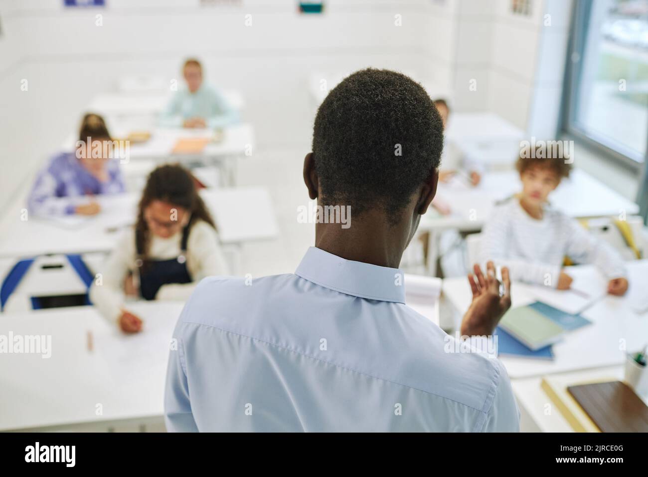 Minimale Rückansicht des männlichen Lehrers, der zu verschiedenen Gruppen von Kindern in der Klasse geht Stockfoto