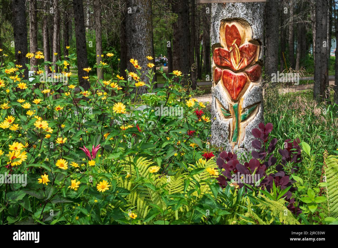 Eine Blumenholzschnitzerei auf einem Totempfahl in einem Blumengarten im Riding Mountain National Park, Manitoba, Kanada. Stockfoto