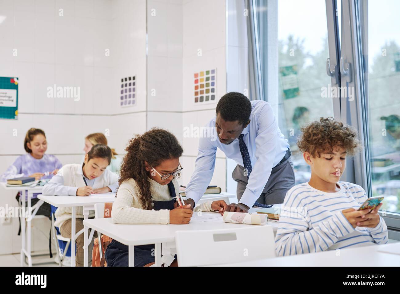Porträt eines schwarzen männlichen Lehrers, der mit Kindern arbeitet, die im Klassenzimmer einen Test machen Stockfoto