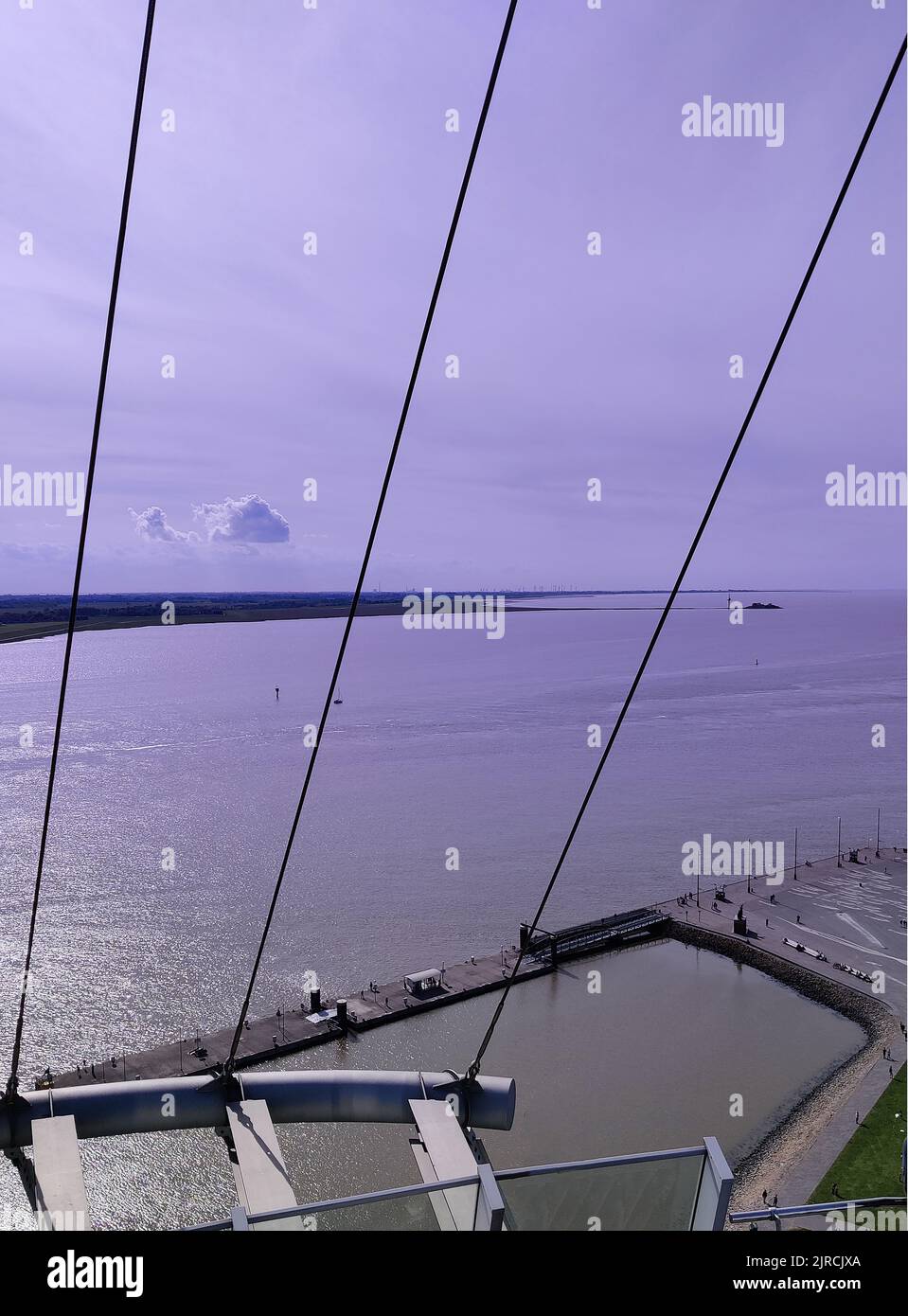 Eine vertikale Aufnahme des Ozeans von einer Brücke mit Aufhängekabeln, wobei der Himmel violett leuchtet Stockfoto