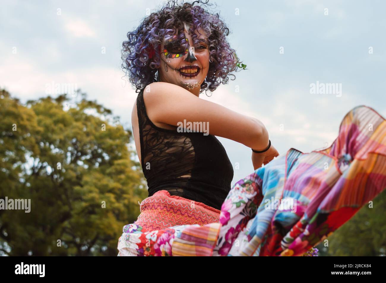 Lateinische junge Frau mit La Calavera Catrina Make-up, in einem langen Rock gekleidet, tanzt im Freien traditionelle Tänze. Stockfoto