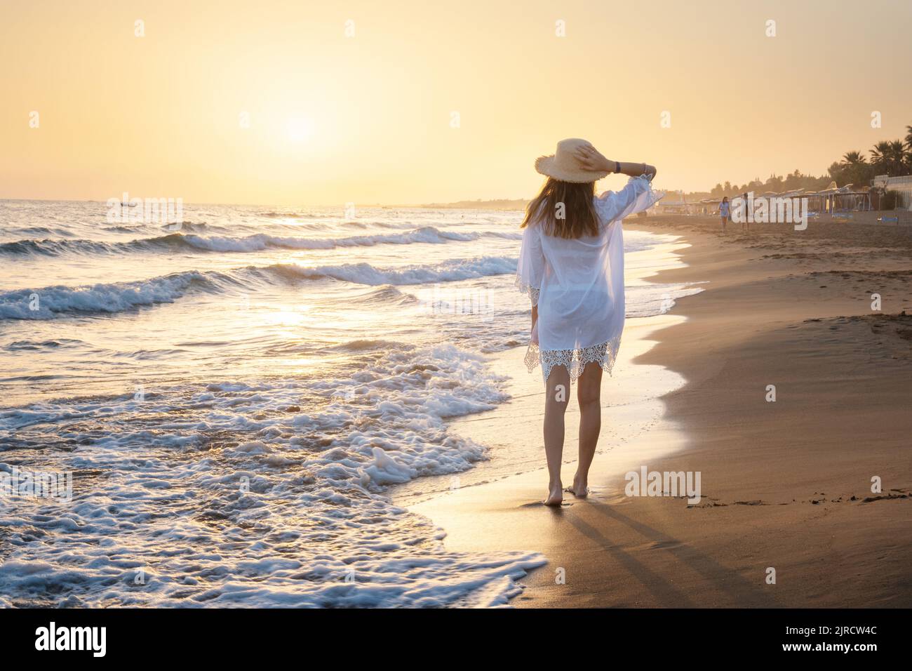 Schöne junge Frau mit Strohhut in weißem Kleid auf dem Meer Stockfoto