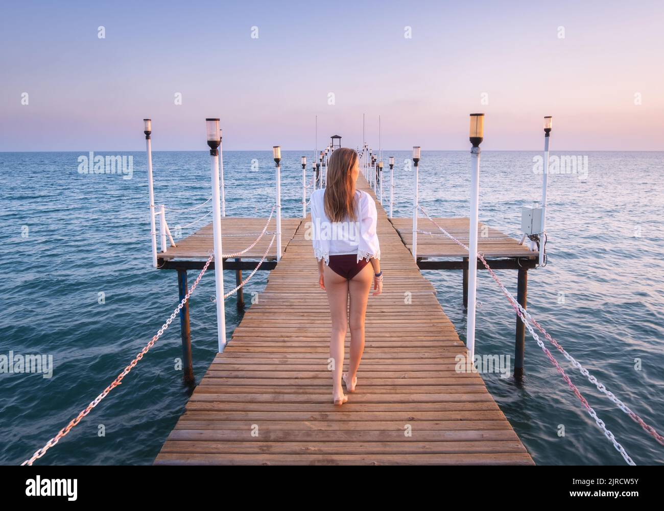 Glückliche junge Frau im Bikini, die auf dem hölzernen Pier am Meer läuft Stockfoto