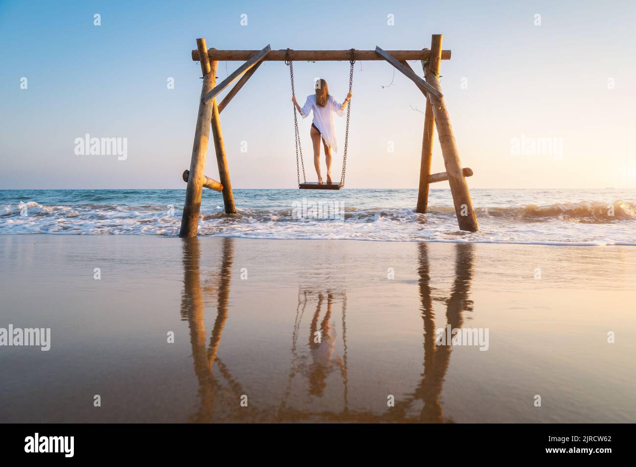 Glückliche junge Frau auf hölzerner Schaukel im Wasser, schönes blaues Meer Stockfoto
