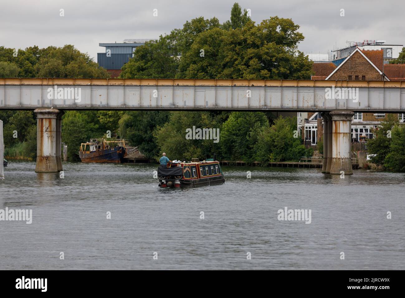 Ein traditionelles englisches Binnenschiff fährt am Sommertag entlang der Themse unter der Eiseneisenbahn-Brücke in Staines upon Thames Stockfoto