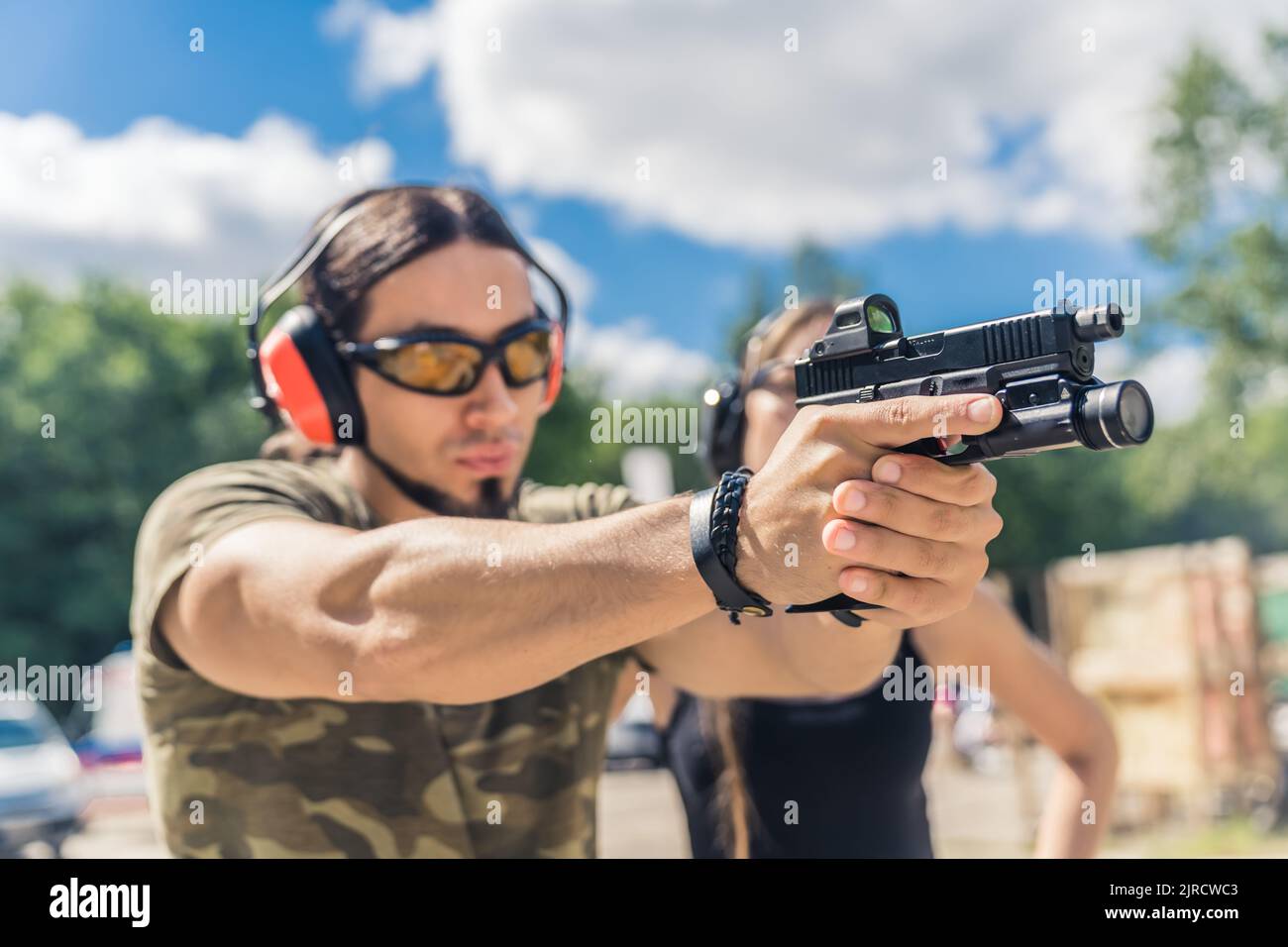 Kaukasischer bärtiger Mann in Sicherheitsausrüstung und Tarnkleidung mit Zielhandwaffe. Schusswaffentraining auf dem Schießstand im Freien. Horizontale Aufnahme. Hochwertige Fotos Stockfoto