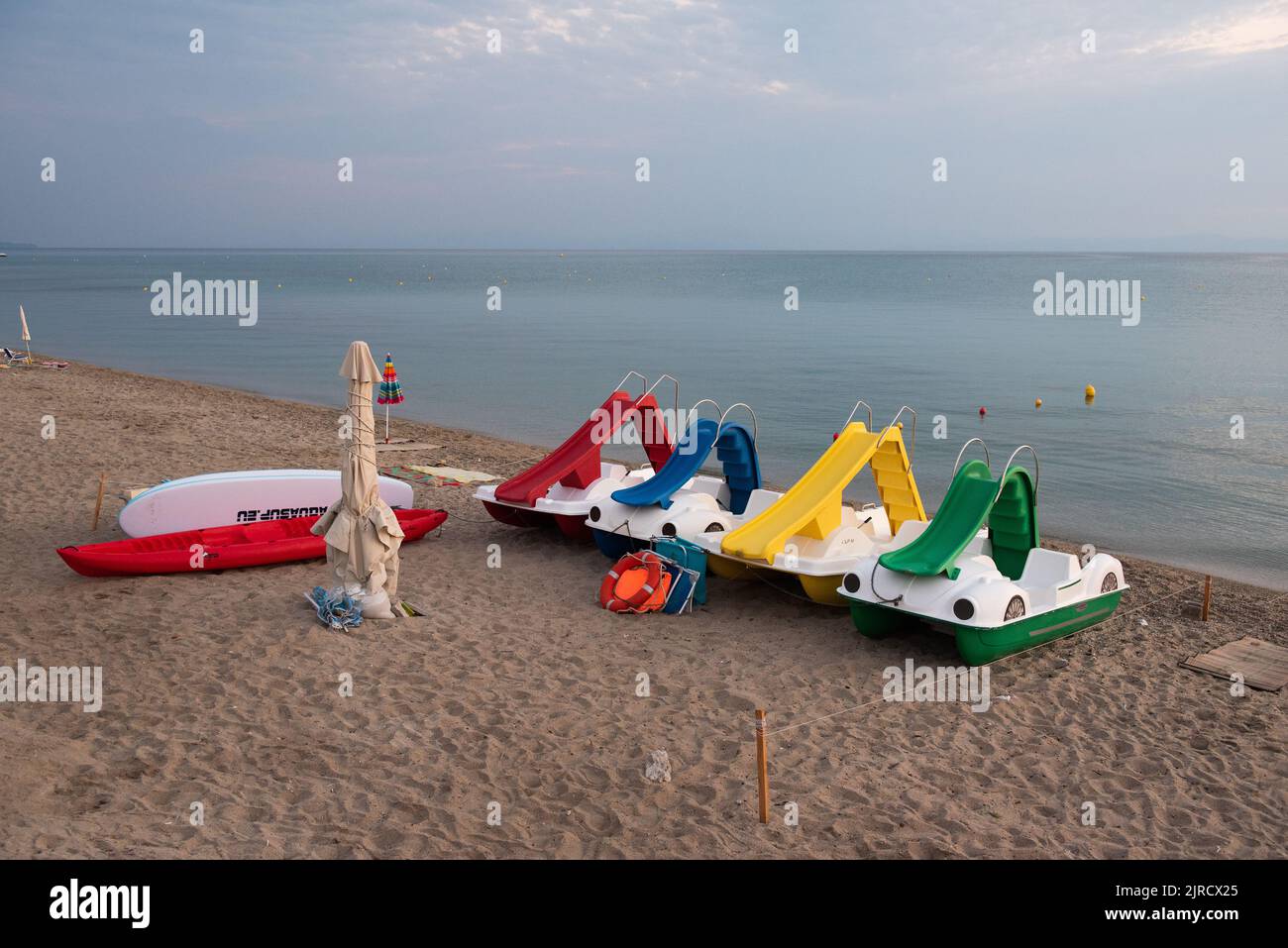 Leere Tretboote zu Beginn des Tages warten auf einen Strand mit ruhigem blauem Meer. Sie warteten am Anfang des Tages in der Schlange. Stockfoto