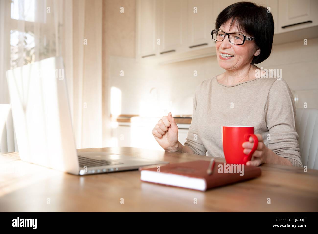 Ein glücklicher, anspruchsvoller Videoanruf einer älteren Frau auf einem Laptop, der von zu Hause aus läuft. Eine lächelnde Frau spricht Mitte 60s in einem virtuellen Online-Konferenzchat Stockfoto