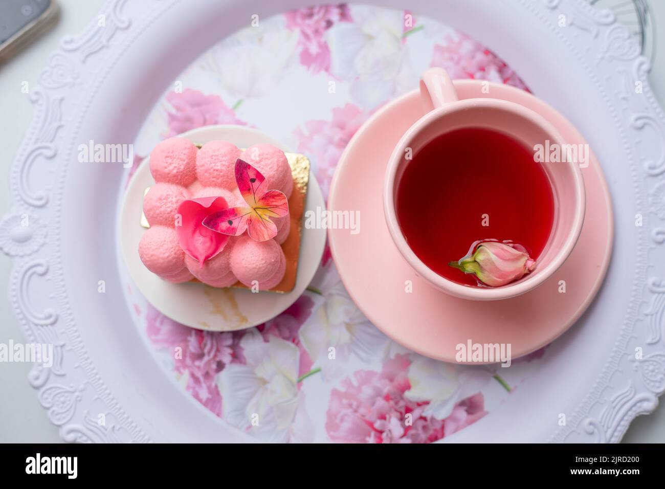 Sugar Sweet Pink Cube Ball Velours Mousse Kuchen Dessert mit Schmetterling Dekoration auf dem Teller und eine Tasse Tee mit Rose Knospe Stockfoto