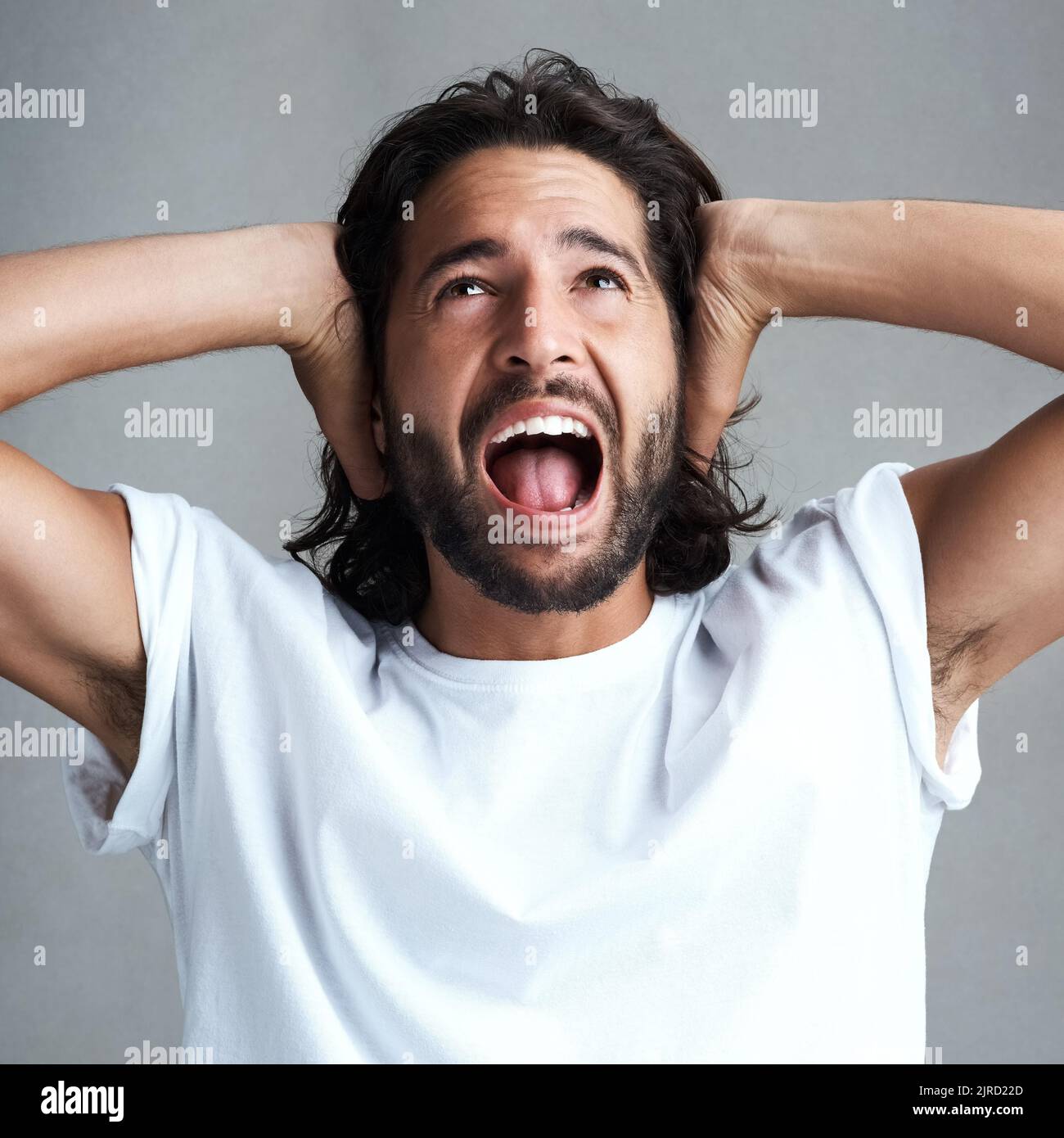 Der die Musik so laut aufdrehte. Studioaufnahme eines jungen Mannes, der vor grauem Hintergrund schreit. Stockfoto