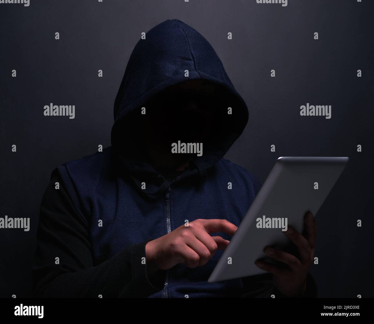 Wer sollte mein nächstes Opfer sein. Ein nicht erkennbarer Hacker, der ein digitales Tablet vor dunklem Hintergrund nutzt. Stockfoto