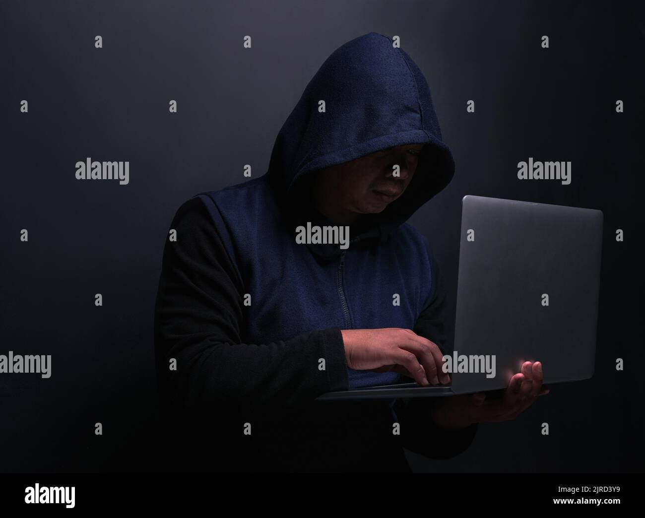 Hacker sind die Meister der Tarnung. Ein nicht erkennbarer Hacker, der einen Laptop vor dunklem Hintergrund nutzt. Stockfoto