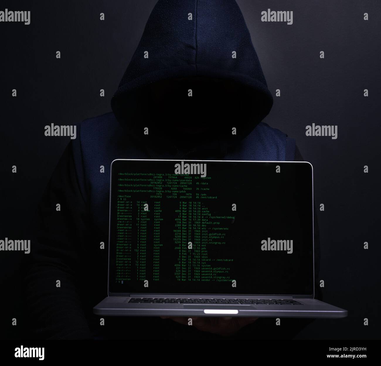 Im Stealth-Modus. Porträt eines nicht erkennbaren Hackers, der einen Laptop vor einem dunklen Hintergrund hochhält. Stockfoto