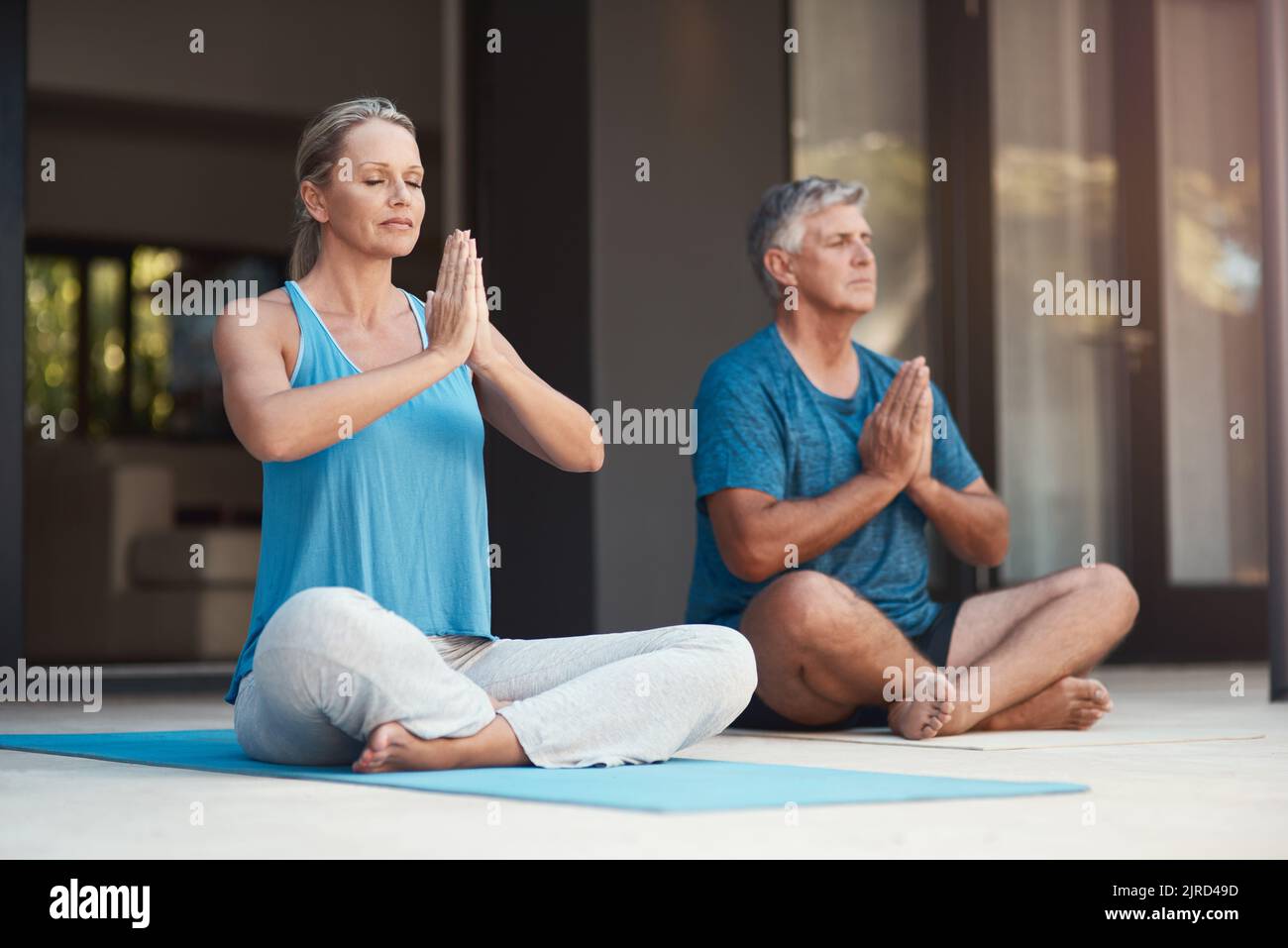 Friedliche Geister sind glückliche Geister. Ein reifes Paar tritt friedlich in eine Yoga-Pose mit gekreuzten Beinen und zusammengesteppten Händen ein. Stockfoto