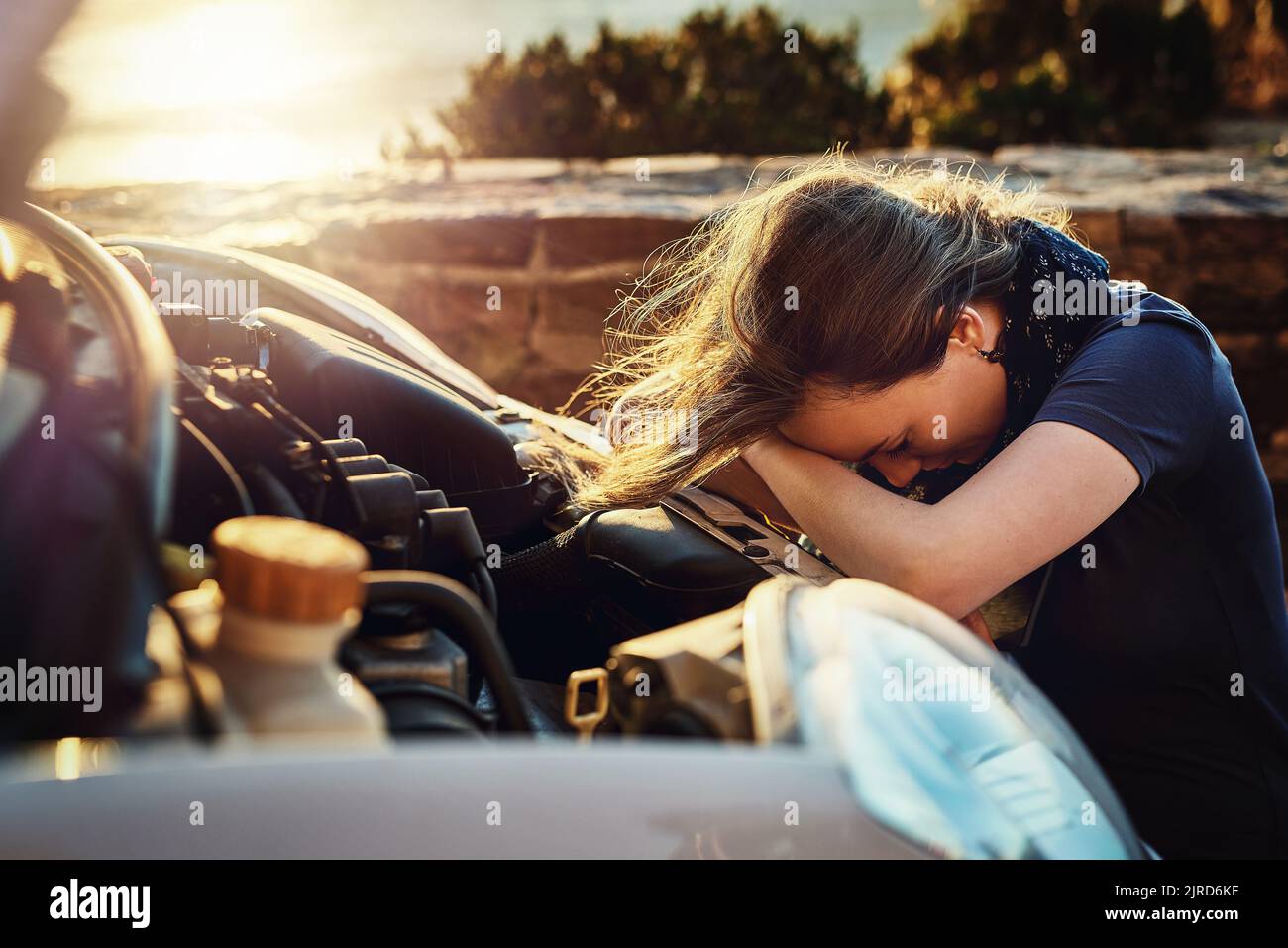 Sowohl sie als auch ihr Auto durchmachen einen Zusammenbruch. Eine junge Frau, die aufgeregt aussieht, nachdem sie am Straßenrand zusammengebrochen ist. Stockfoto