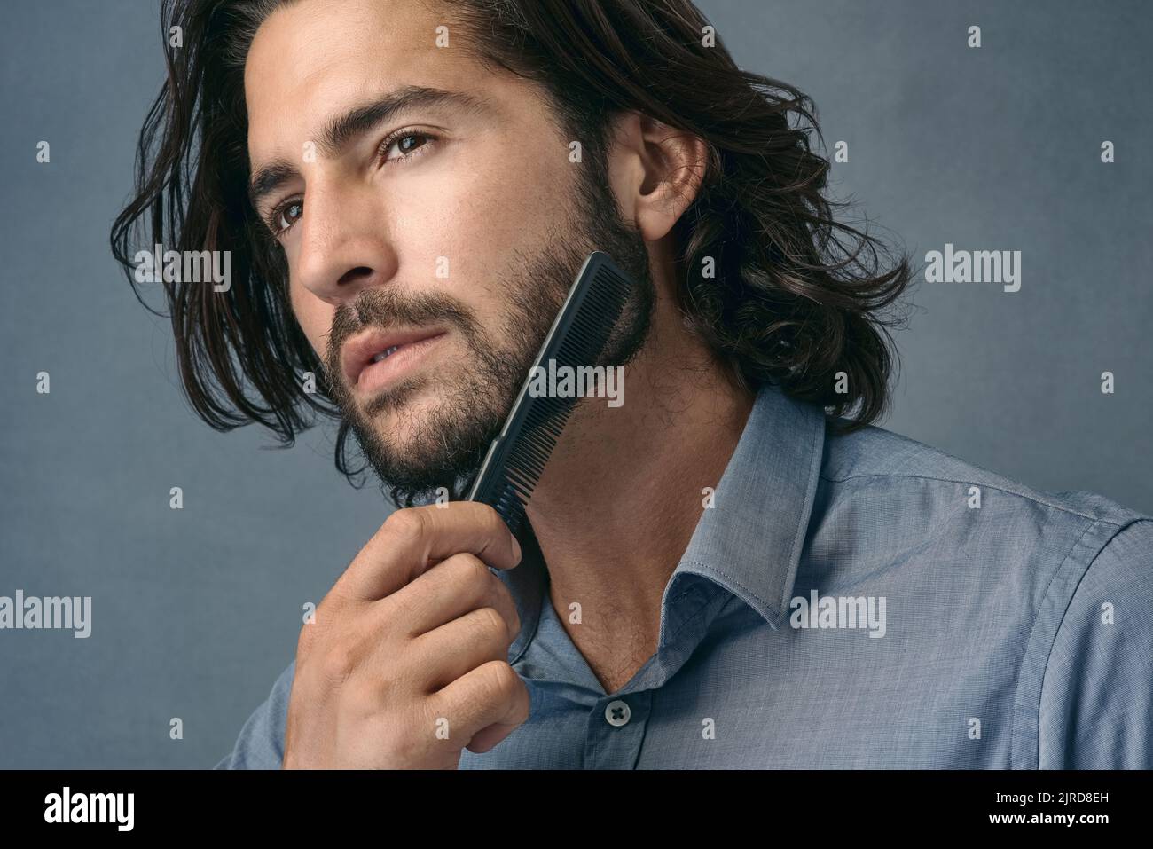 Den bärtigen Look lieben. Studioaufnahme eines hübschen jungen Mannes, der seinen Bart vor einem grauen Hintergrund kämmt. Stockfoto