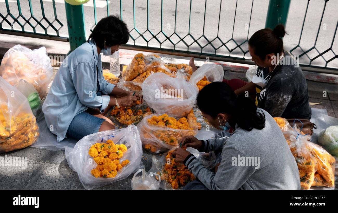 Damen, die gelbe Blumenkränze vor dem Erawan-Schrein auf der Rama 1 Road Bangkok Thailand machen Stockfoto