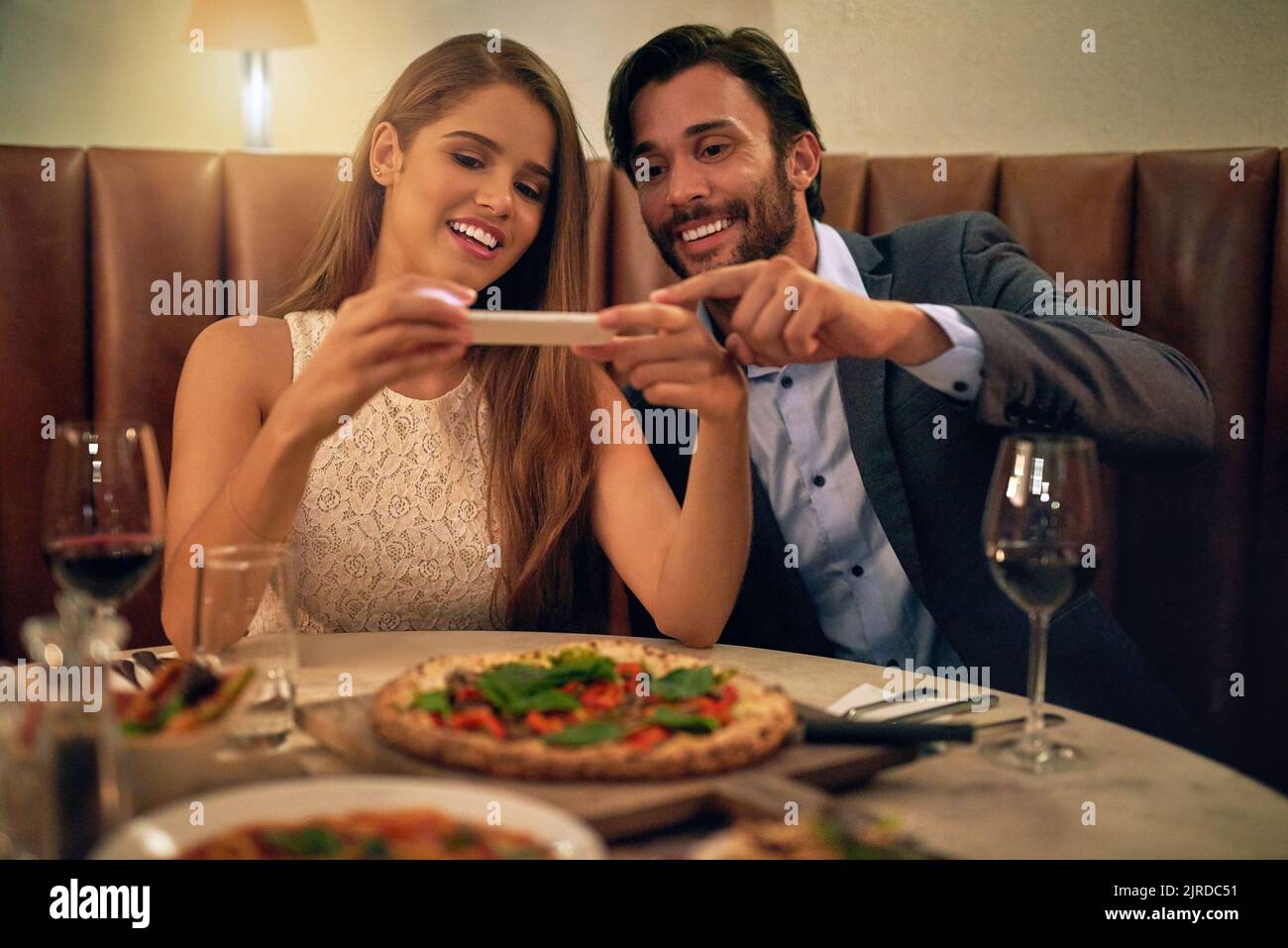 Ein glückliches junges Paar, das während eines romantischen Abendessens in einem Restaurant ein Foto von seinem Essen auf einem Handy macht. Stockfoto
