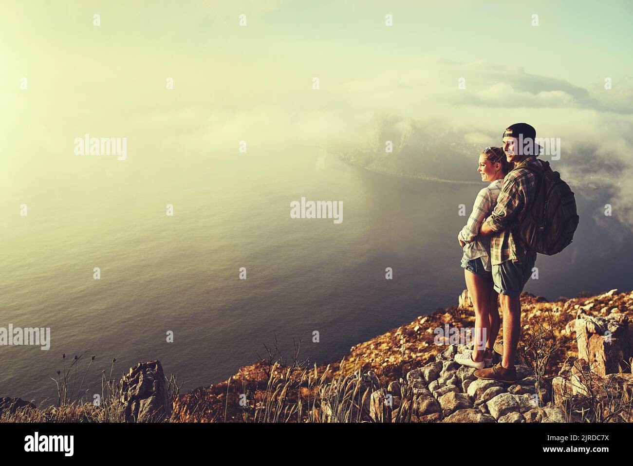 Entdecken Sie die Liebe in der freien Natur. Ein abenteuerliches junges Paar, das während einer Wanderung die Aussicht von einem Berggipfel bewundert. Stockfoto