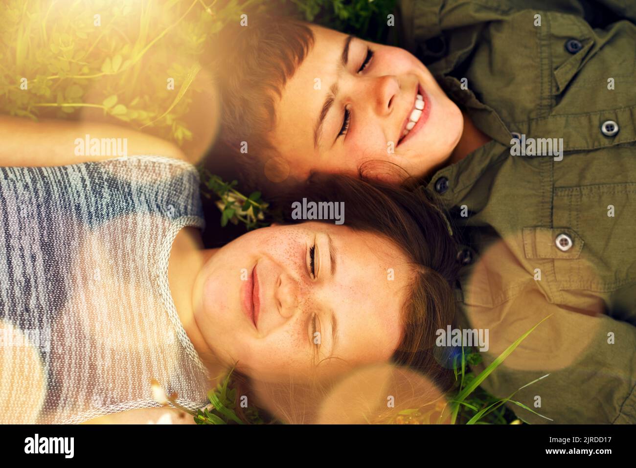 Fröhliche Sommerträume. Zwei niedliche Geschwister liegen draußen auf dem Gras nebeneinander. Stockfoto