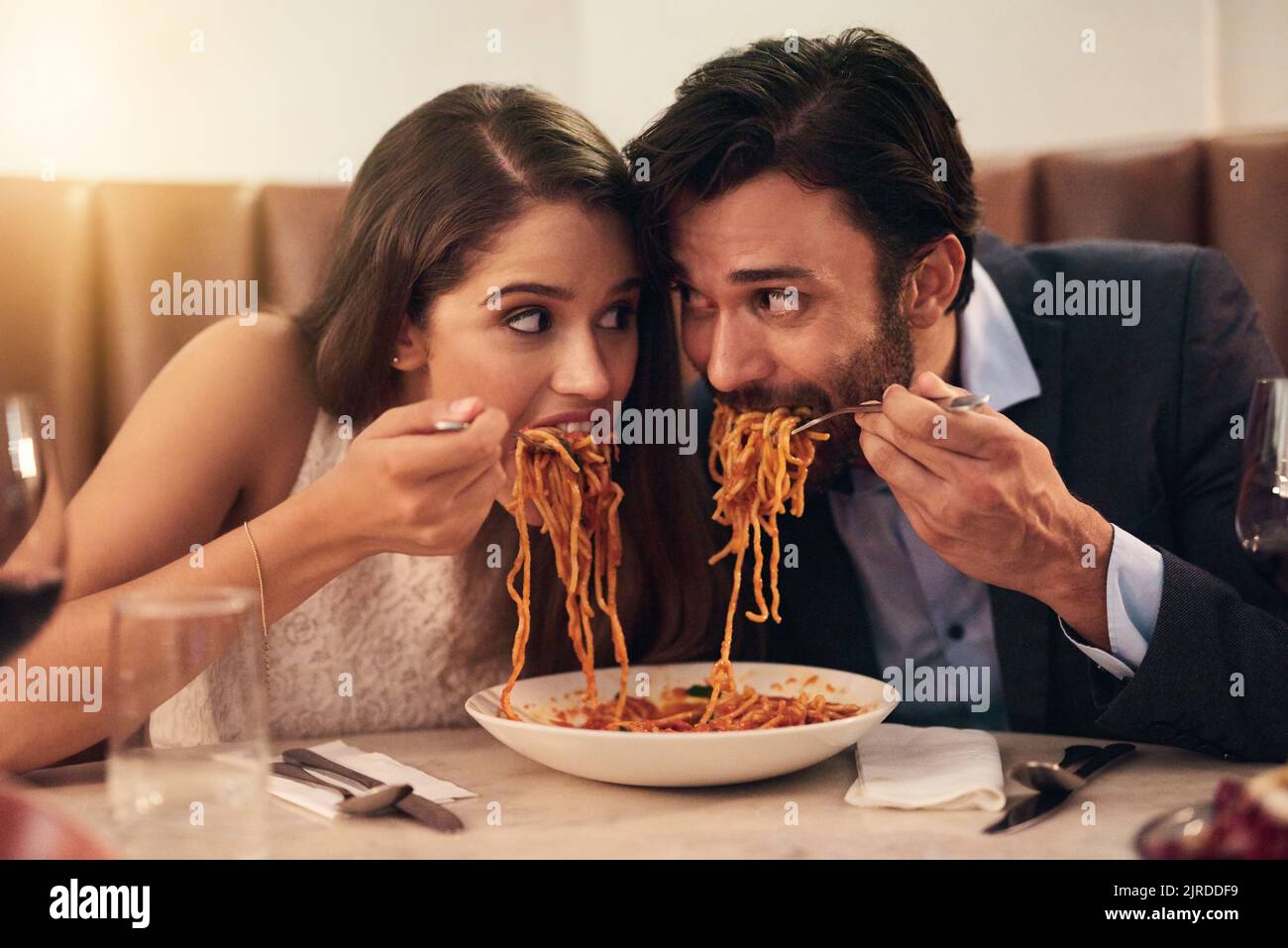 Ein junges Paar teilt sich einen Teller mit Spaghetti während eines romantischen Abendessens in einem Restaurant. Stockfoto