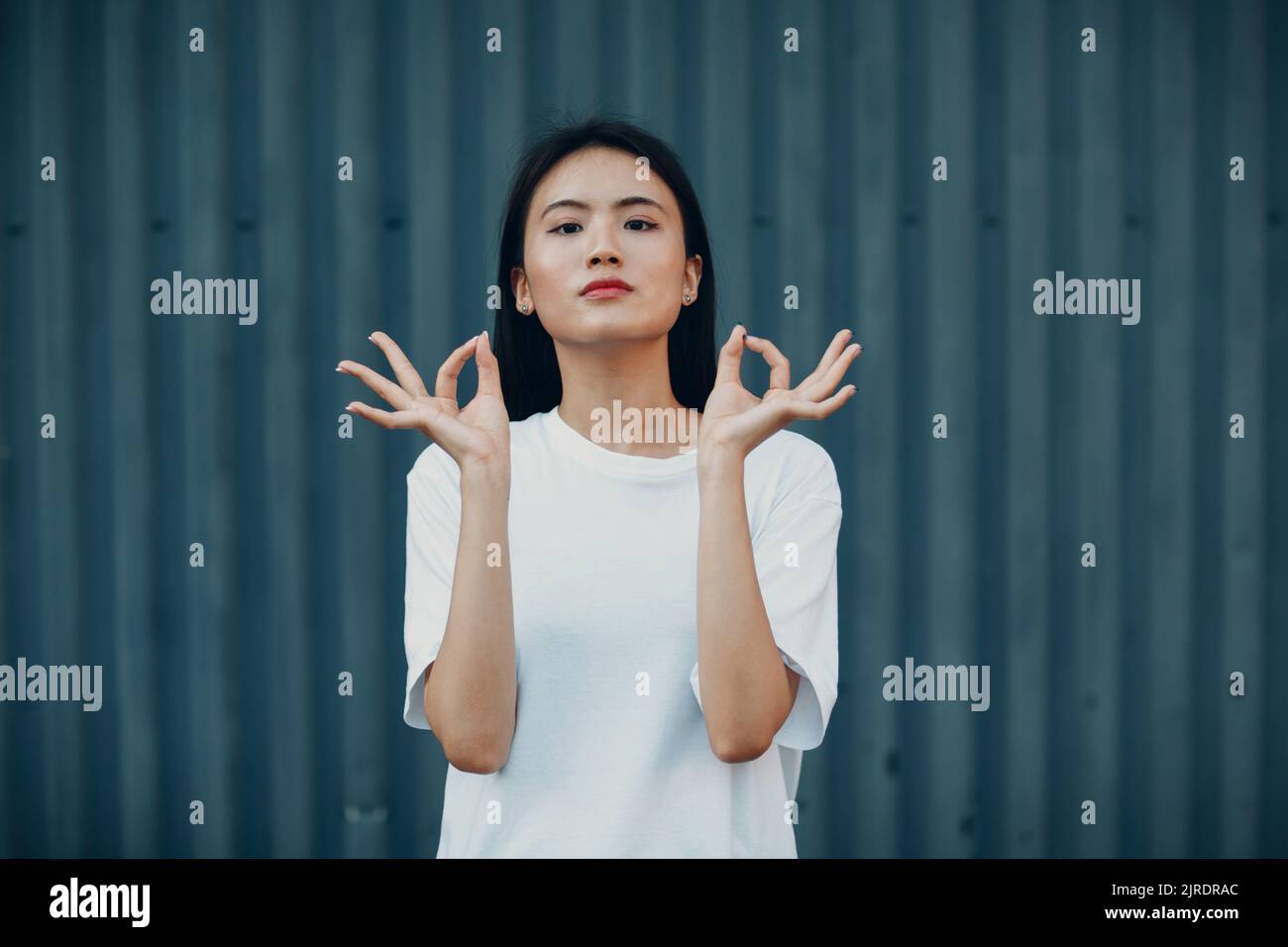 Porträt einer asiatischen Frau mit der Hand okay Gestik gegen blaue Wand Stockfoto