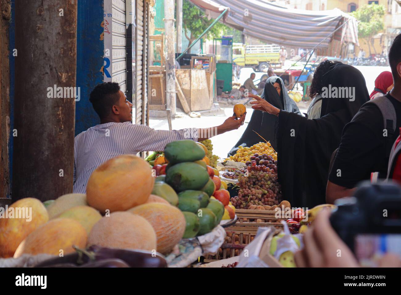 ESNA, LUXOR, ÄGYPTEN - 13. AUGUST 2022: Verschleierte Frauen in traditioneller schwarzer Kleidung kaufen Früchte auf dem lokalen Markt in der Stadt Esna, südlich von Luxor. Stockfoto