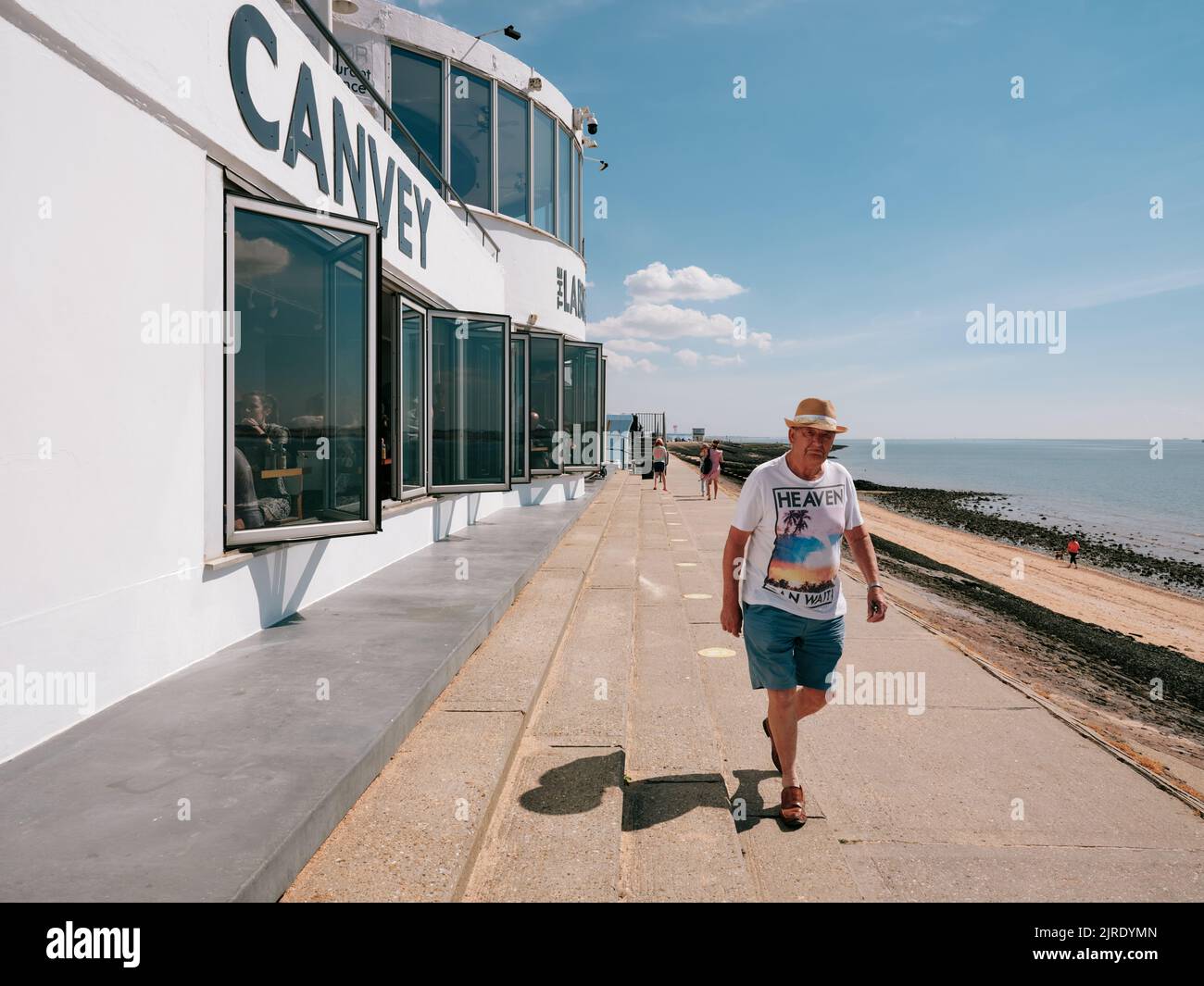 Sommermann mit Himmelshemd, der am modernistischen Labworth Cafe vorbeiging, Canvey Island, Thames Estuary, Essex, England, Großbritannien - Sommerleben Stockfoto