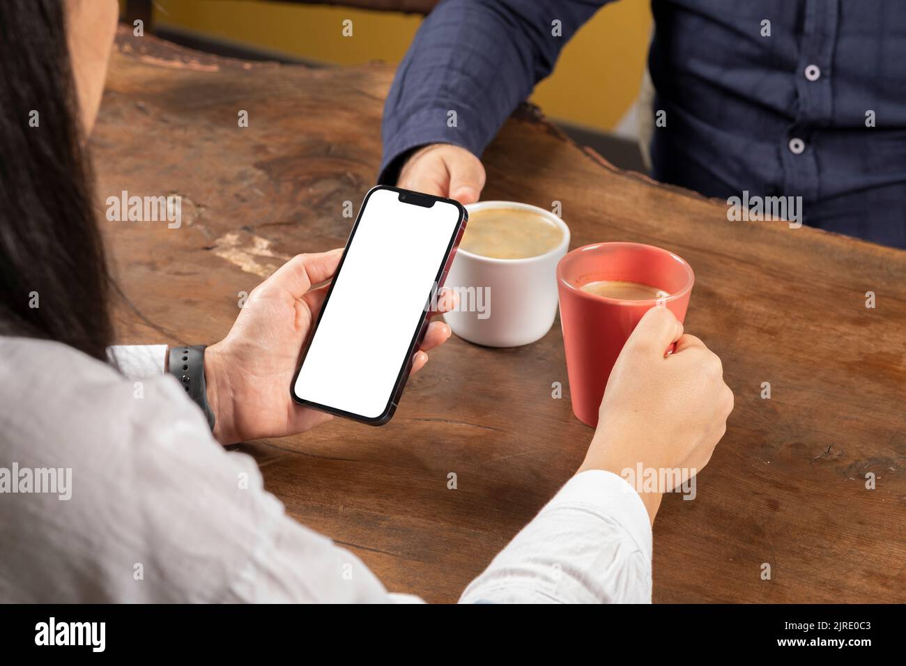 Smartphone halten, Frau auf dem Holztisch sitzen und Smartphone halten. Paar Dating im Café, junge Frau ignoriert Mann. Weißer Bildschirm. Stockfoto