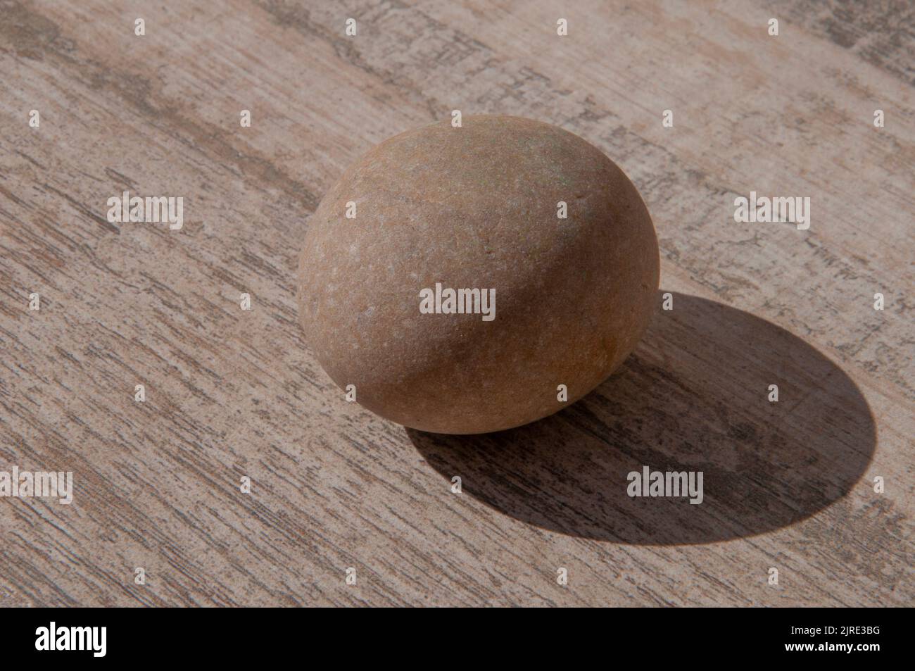 Glatte graue Steinkugel über Stein oder Holz wie Hintergrund mit Schatten Stockfoto