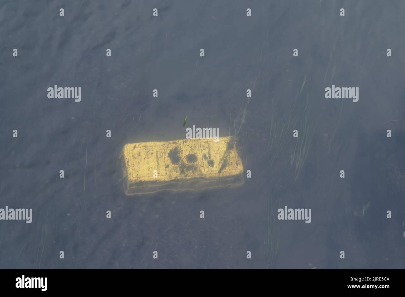 Ein gelber Ständer oder eine Schachtel aus Kunststoff wurde ins Wasser geworfen und dem Zerfall überlassen Stockfoto