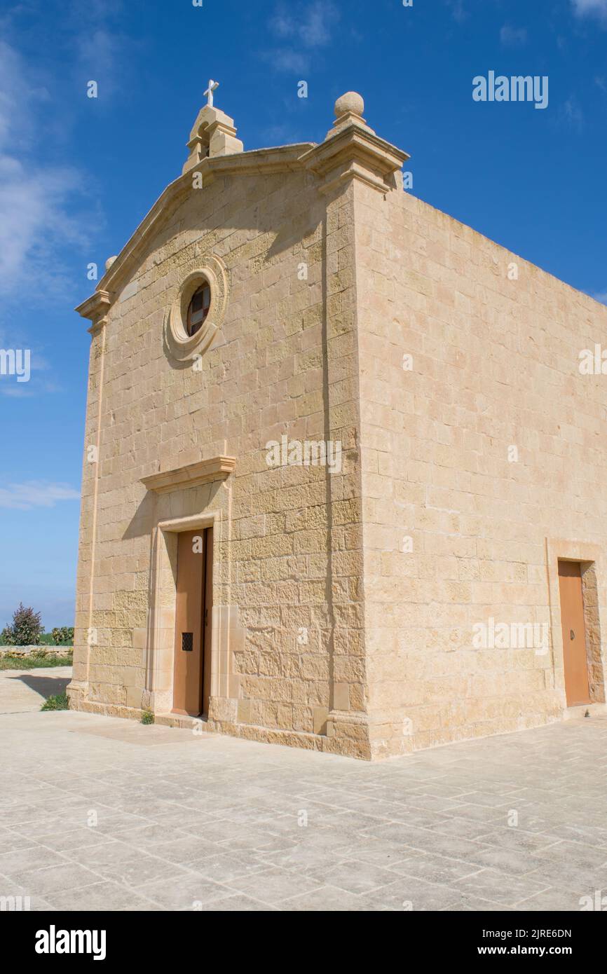 Die aus Kalkstein isolierte historische katholische Kapelle von Saint Dimitri, in der Landschaft von Gharb, Gozo, Malta. An einem bewölkten Frühlingstag, mit blauem Himmel. Stockfoto