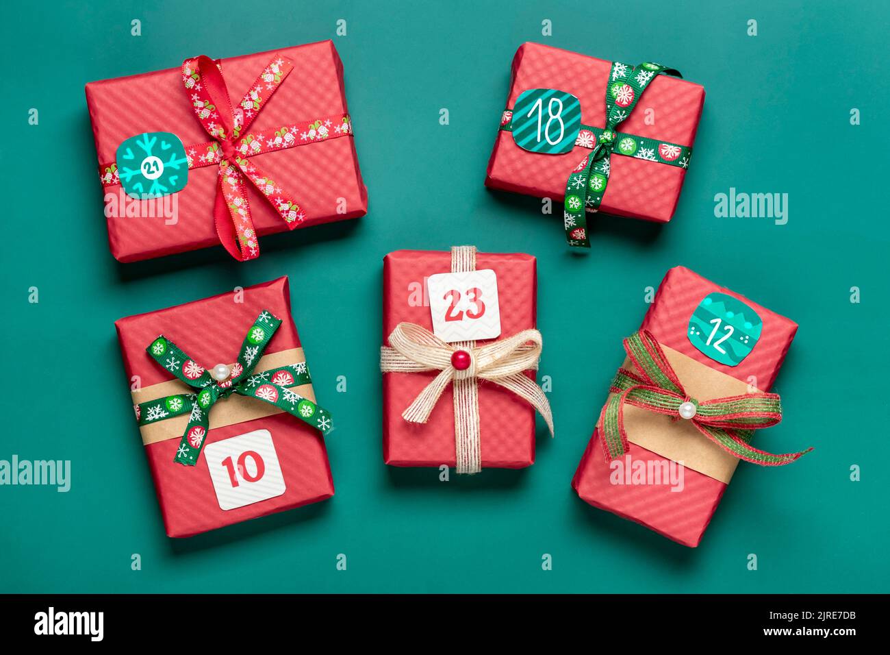 Adventskalender Handgewickelte rote, grüne Geschenkschachteln mit Bändern, Schneeflocken und Zahlen, Weihnachtsschmuck und Dekor auf grünem Tisch Stockfoto