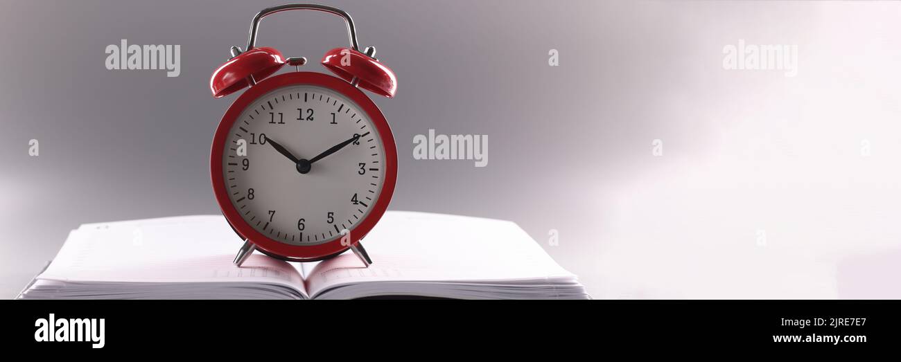 Roter Retro-Uhrenständer auf offenem Notizbuch oder Buch Stockfoto