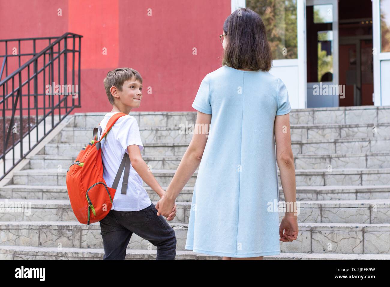 Eine Mutter und ein Kind, ein Junge mit einem Schulrucksack, steigen die Treppe zur Schule. Mutter bringt Sohn zur Schule. Mutter bringt Sohn zur Schule. Stockfoto