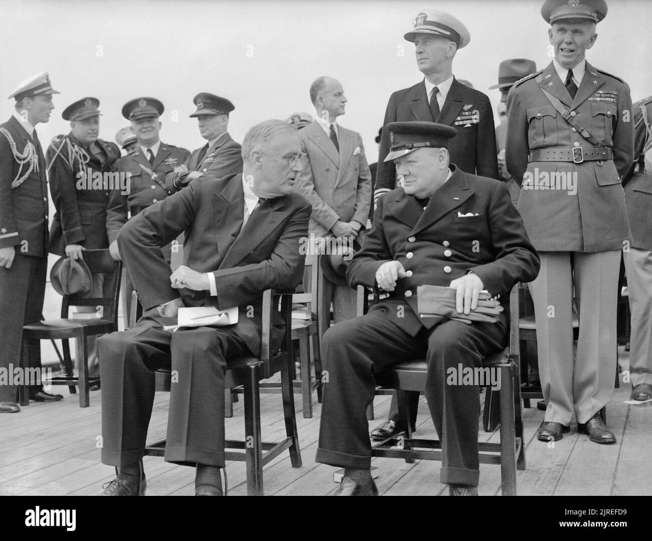 Präsident Roosevelt und Winston Churchill sitzt auf dem Achterdeck der HMS Prince of Wales für einen Sonntag Service während der atlantischen Konferenz, 10. August 1941. Der Präsident der Vereinigten Staaten, Franklin D Roosevelt und der britische Premierminister Winston Churchill sind auf dem Achterdeck der HMS Prince of Wales sitzt. Sie unterhalten sich nach einem Sonntag Service während der atlantischen Konferenz, 10. August 1941. Unmittelbar hinter ihnen sind Admiral E J König, USN und General Marshall, US Army. Der Präsident Söhne, Fähnrich Franklin Roosevelt jr USNR und Kapitän Elliot Roosevelt USAA Stockfoto
