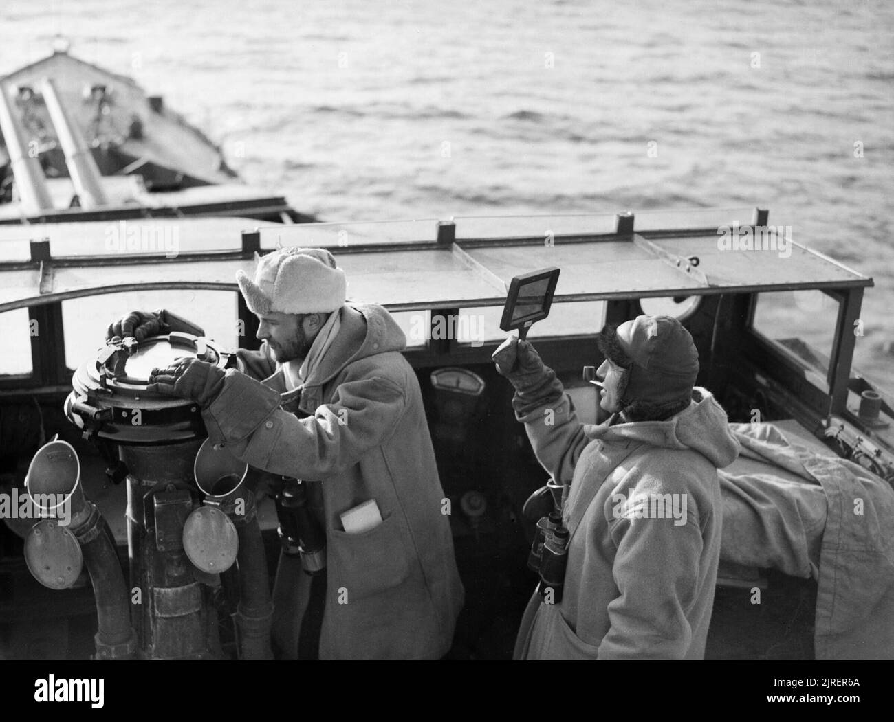 Die Offiziere auf der Brücke von HMS LEGION während des Überfalls auf den Lofoten in Norwegen, 5. März 1941. Der erste Lieutenant der Zerstörer HMS LEGION, Lieutenant Cartwright, nimmt ein Lager, während der Captain, Commander Jessel, schauen hält für feindliche Flugzeuge, wie das Schiff im Westen Fjord bei einer Razzia auf den Lofoten verlässt. Beide Männer sind mit dicken Winterkleidung und Jessel ist mit einem Getönte einige der Blendung der Sonne zu blockieren. Stockfoto