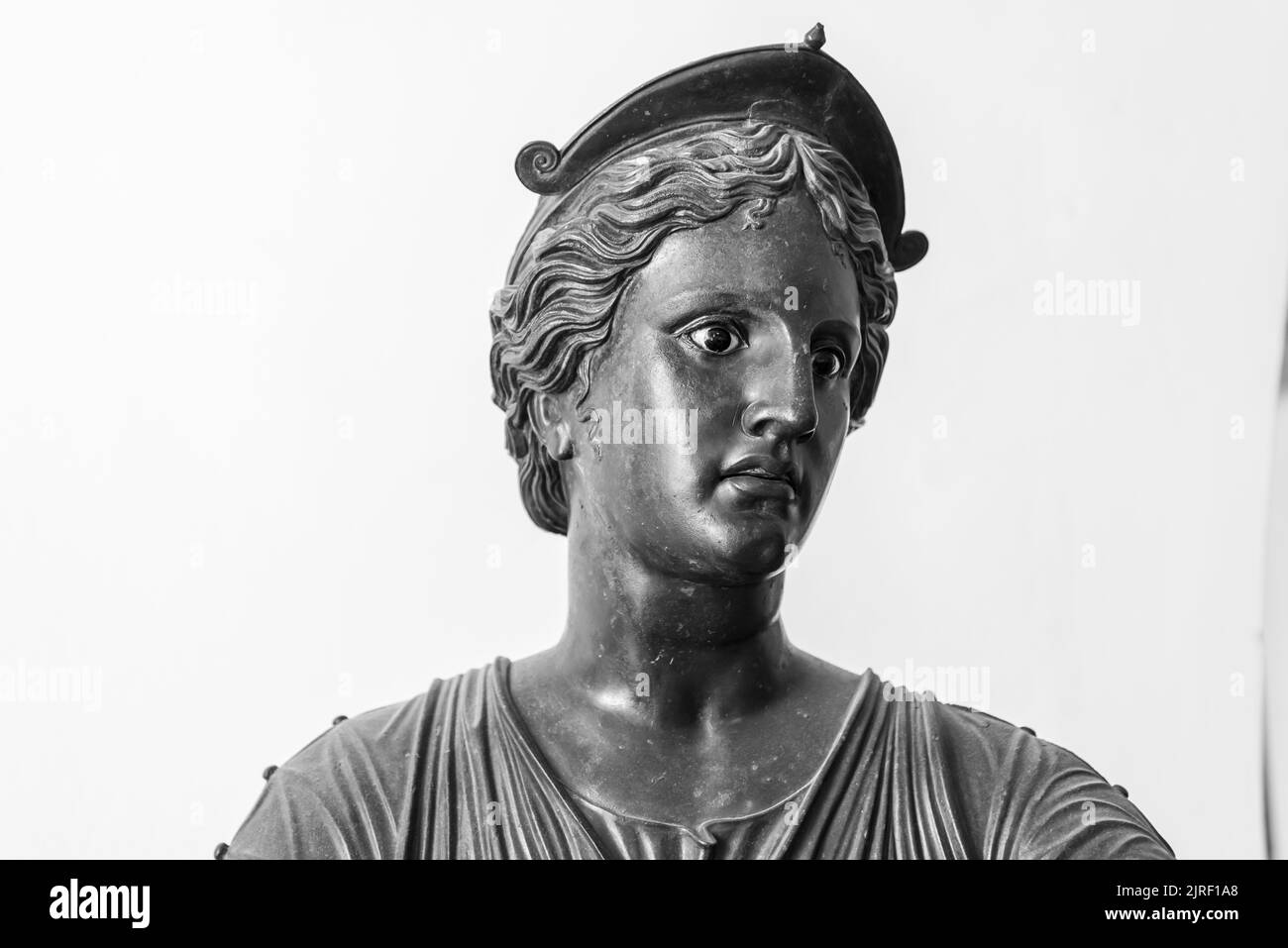 Schwarz-Weiß-Foto, das in Nahaufnahme das Gesicht einer alten Metallstatue zeigt, die eine junge römerin mit einem Hut darstellt Stockfoto