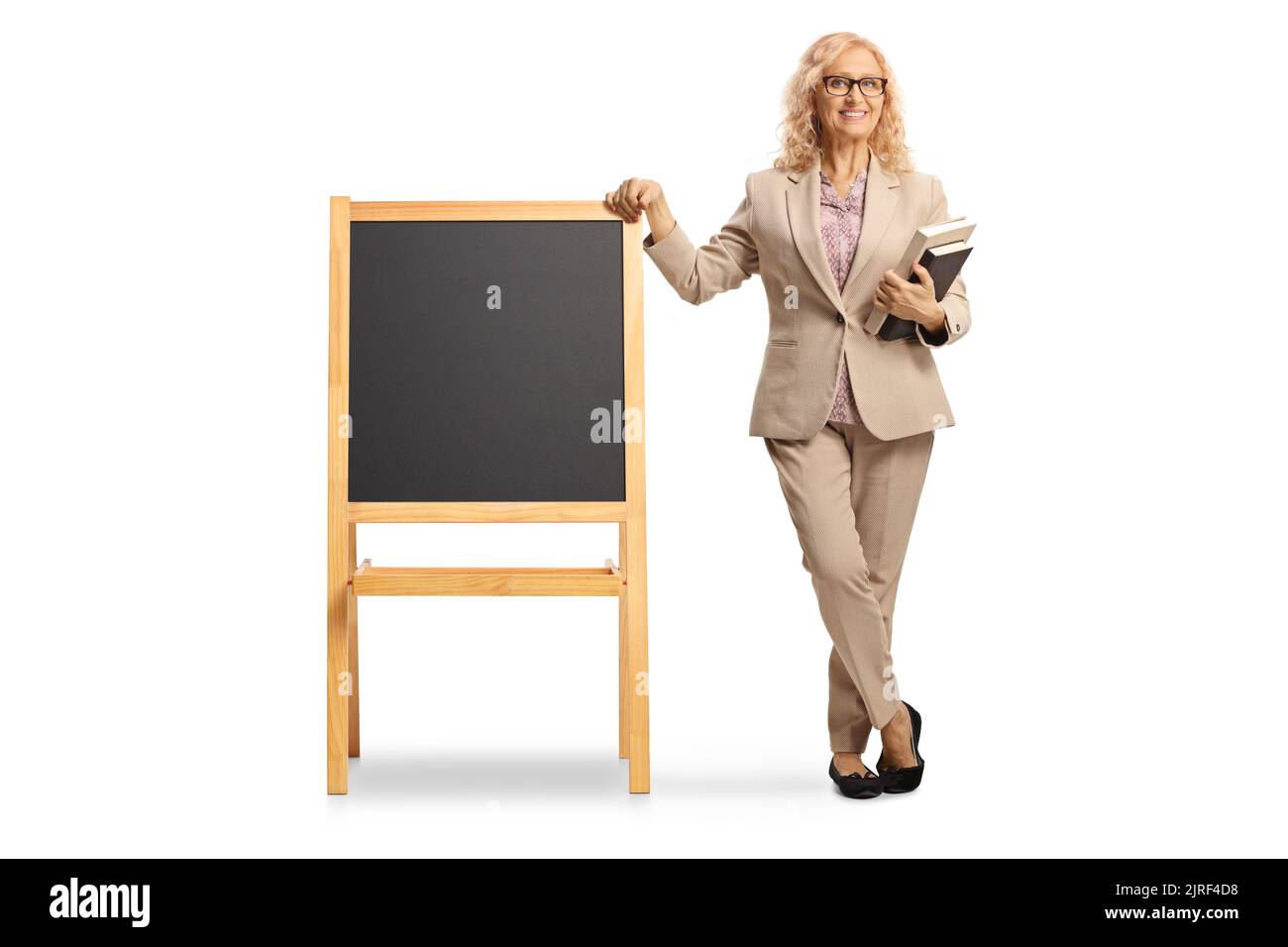 In voller Länge Porträt einer reifen Lehrerin, die neben einer Tafel auf weißem Hintergrund isoliert steht Stockfoto