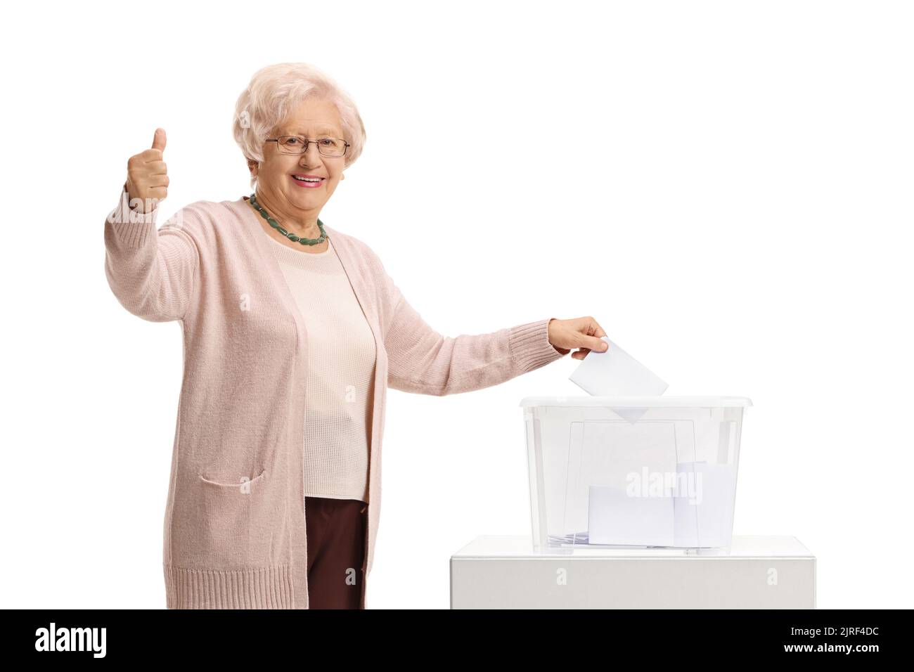 Eine ältere Dame, die in einer Wahlurne abstimmen und auf weißem Hintergrund die Daumen nach oben zeigen kann Stockfoto