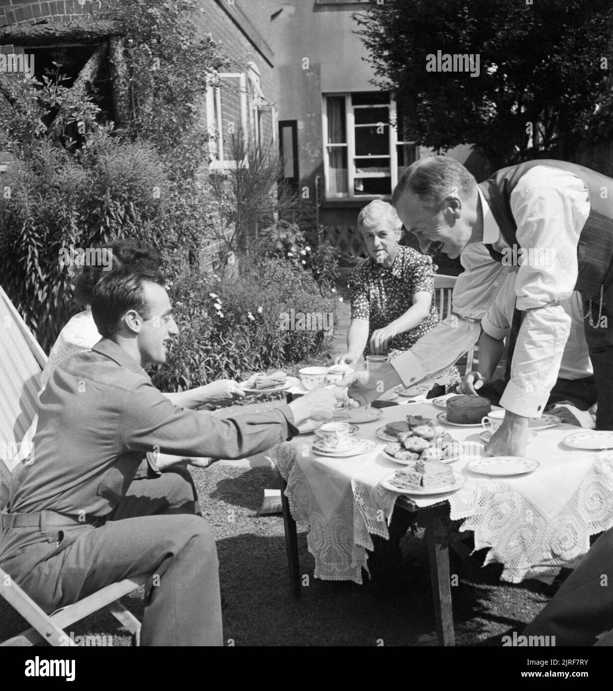 Ein US-Soldat in Tee mit ex-Bürgermeister von Winchester, Herr Edmonds, und seine Frau und seine Tochter im Garten ihres Hauses während 1944. Alfred Miraglia (links, aus New York) dauert Kaffee in der Sonne mit der ex-Bürgermeister von Winchester Herr Edmonds und seine Frau und seine Tochter im Garten ihres Hauses. Die Legende besagt, dass die Edmonds' Kinder, Roger (nicht abgebildet) und Betty, die uns als Gäste der Bürgermeister von Winchester, Virginia eingeladen wurden, und erhielt später einen Teil ihrer Ausbildung dort. Stockfoto