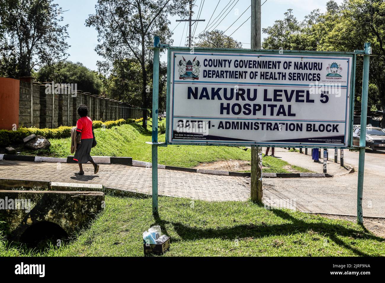 Eine Frau kommt an einer Schild-Tafel des Nakuru Level 5 Krankenhauses in der Stadt Nakuru vorbei, wo zwei Kinder, die vom Schweinegrippe-Virus (H1N1) betroffen sind, aufgenommen werden. Die Regierung sagt, dass sie einen Ausbruch der Schweinegrippe (H1N1) im Dorf Kiptangwanyi eingedämmt hat. Die Viruserkrankung hat das Leben eines Kindes beansprucht und 8 weitere im Nakuru Level 5 und im Kiptangwanyi Health Center in Elementtaita ward aufgenommen. Stockfoto
