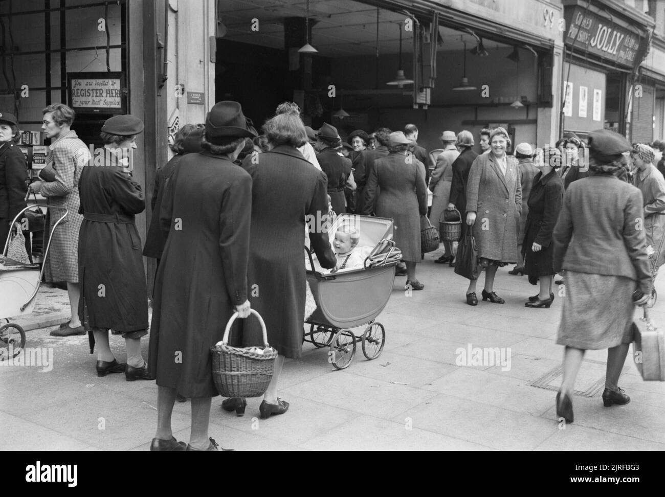 Käufer Warteschlange für Gemüse außerhalb der Gemüsehändler Shop, 'J Holz", 97-99 High Road, Wood Green, London 1945. Massen von Frauen, die das Pflaster, wie sie für Gemüse außerhalb der Gemüsehändler shop Queue, 'J Holz", 97-99 High Road, Holz Grün. Viele haben Babys im Kinderwagen. Gerade sichtbar rechts auf dem Foto ist der Shop 'Jolly', die verkauft" zubereitet Bestimmungen fertig auf dem Tisch, wie zum Beispiel Torten, Gebäck und Sandwiches. Stockfoto