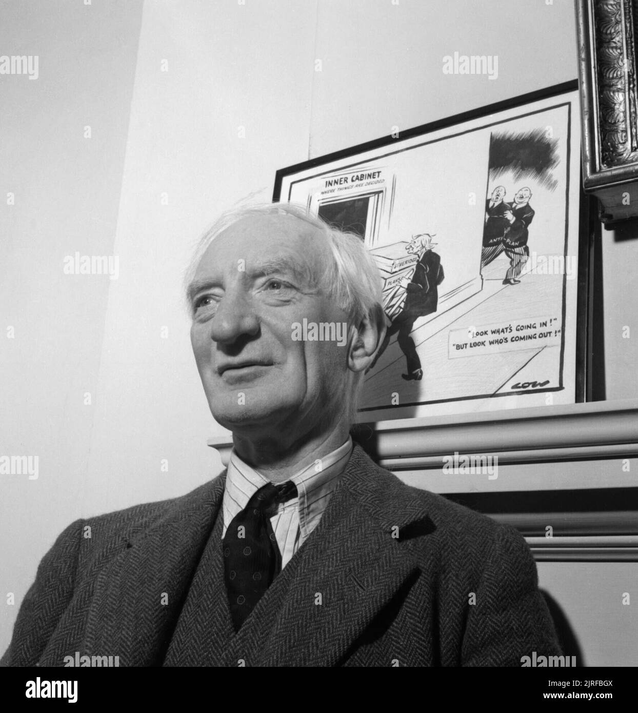 Sir William Beveridge in seiner Studie an der Universität Oxford, 1943. Ein Kopf und Schultern Portrait von Sir William Beveridge in seiner Studie an der Universität Oxford. Er steht vor einer Karikatur von Niedrigen zu seinem Bericht über die soziale Wohlfahrt. Stockfoto