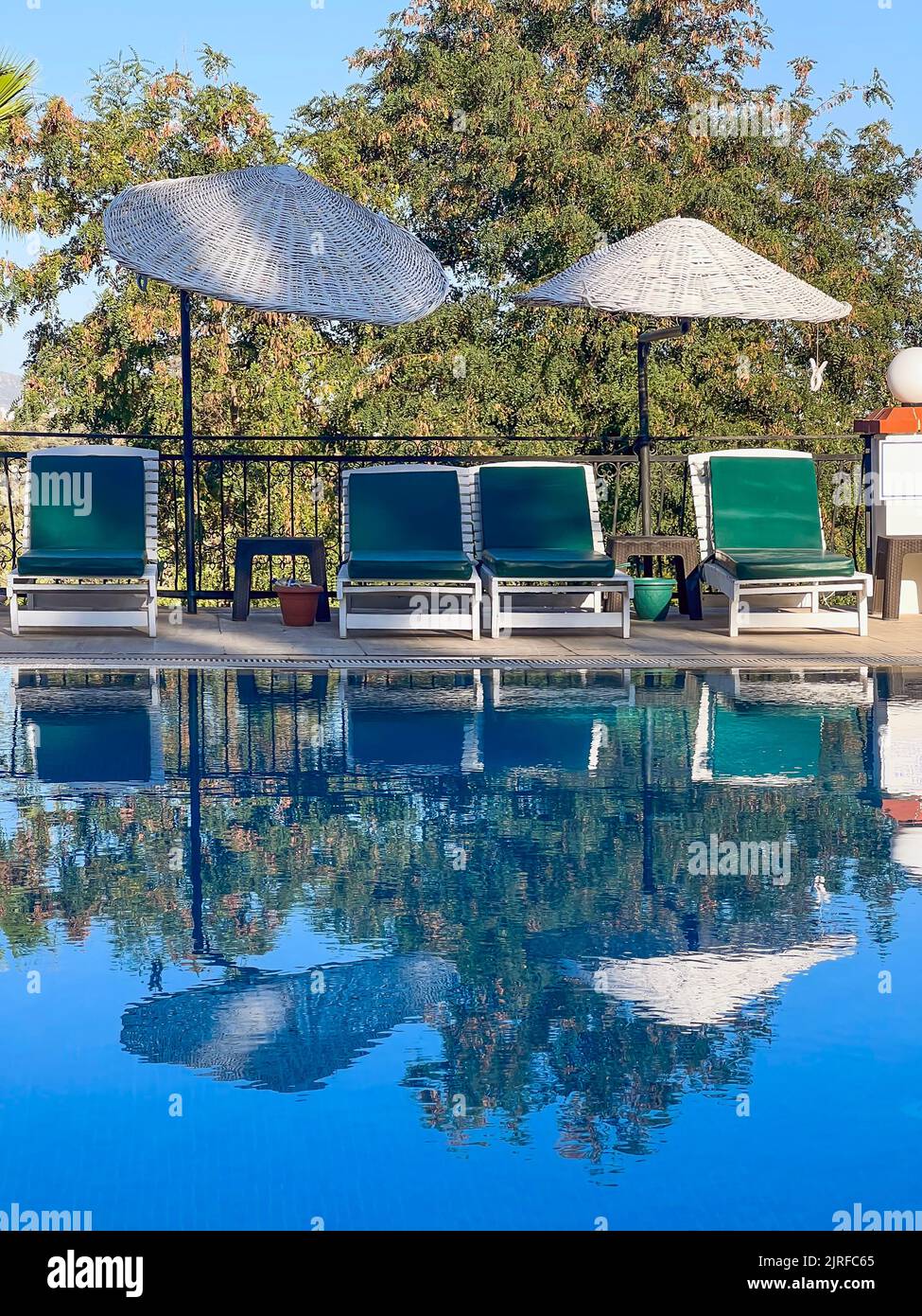 Leere Liegestühle und Sonnenschirme am Pool. Sommerurlaub Hintergrund mit Kopierplatz. Klares Wasser, das die Umgebung reflektiert Stockfoto