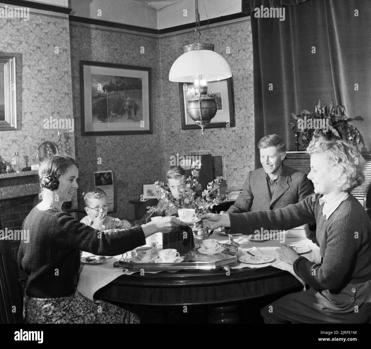 Kampf der Land - die Arbeit der Women's Land Army auf dem britischen Home Front, 1942 Iris Joyce (rechts) nimmt den Tee mit Ihrem neuen Arbeitgeber bei der Ankunft an Ihrem ersten Bauernhof irgendwo in Großbritannien. Am Tisch mit Blende sitzt der Bauer und seine Frau und ihre zwei Söhne. Nach dem ursprünglichen Titel'... müssen Sie Bauernhof Tees wenn Sie auf dem Land" arbeiten! Stockfoto