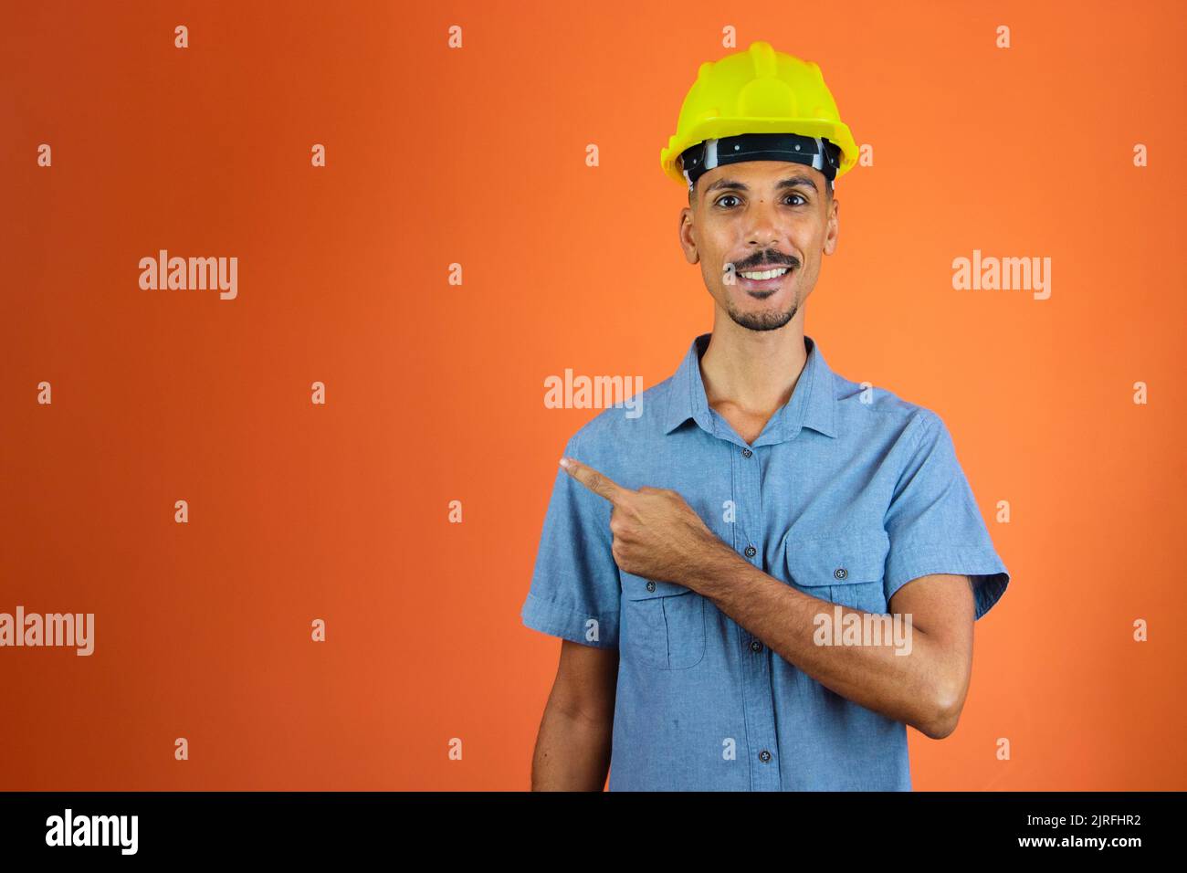 Schwarzer Mann in Sicherheitshelm und blauem Hemd isoliert auf orange. Stockfoto